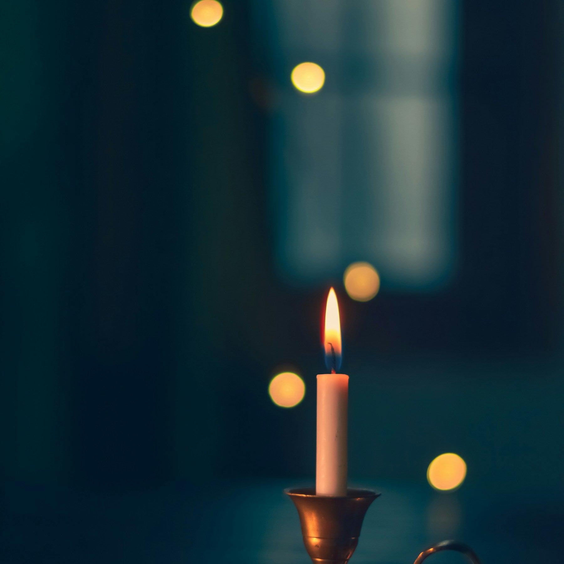 Noma brass taper candle holder glowing against a dark background